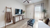 This single-floor residence in Searcy, Arkansas offers a thoughtfully designed layout with a cohesive neutral color palette throughout. The living area is welcoming and comfortable, featuring light wood-look flooring, a ceiling fan, and natural light flowing in through a window with blinds. The space accommodates both a seating arrangement and an entertainment setup, making it practical for everyday living.

The kitchen is a standout feature, showcasing rich dark-stained wood cabinetry paired with light granite countertops for a striking contrast. A central island with bar seating provides additional prep space and casual dining functionality. The kitchen is equipped with full appliances including a range, microwave, dishwasher, and refrigerator, all finished in black. The light flooring carries through from the living area, maintaining a seamless visual flow.

The bedroom is a serene retreat with soft carpet underfoot and neutral walls that contribute to a calm atmosphere. Natural light enters through a window dressed with layered curtains, and the room provides ample space for furnishings.

The bathroom continues the design language of the rest of the home, with dark cabinetry, granite countertops, light flooring, and a full tub-shower combination. The layout is efficient and well-organized, offering practical storage and functionality throughout this Searcy residence.