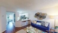 Located in Boca Raton, FL, this well-designed one-bedroom residence offers a thoughtfully organized layout across a single floor. The open-concept living and kitchen area serves as the heart of the home, where warm hardwood-style flooring flows throughout. The kitchen is outfitted with crisp white cabinetry, a mosaic tile backsplash, stainless steel appliances including a refrigerator, range, and microwave, and a bright white quartz peninsula countertop with bar seating — ideal for casual dining or entertaining. A skylight above the kitchen adds a welcome dose of natural light. The adjacent living room is spacious and inviting, featuring a large sliding glass door that fills the area with light and provides access to the exterior. A dedicated hallway connects the living spaces to the private bedroom, which is generously sized and features a walk-in closet, hardwood-style flooring, and a large window dressed with sheer curtains that allow soft, natural light to filter in. A textured ceiling is consistent throughout the home, adding subtle architectural character. The entryway hallway offers additional functional space with track lighting and built-in storage. Overall, this residence presents a clean, modern aesthetic with a bright and airy ambiance throughout.