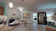 This single-floor residence offers a thoughtfully designed layout that balances comfort and functionality throughout. The open-concept living and dining area serves as the heart of the home, featuring wood-style flooring, a ceiling fan, and sliding doors that open to a private balcony with views of surrounding greenery. A granite-topped breakfast bar connects the dining space to the galley-style kitchen, which is outfitted with warm wood cabinetry, black appliances including an electric range, built-in microwave, and refrigerator, all set atop light tile flooring. The primary bedroom provides a tranquil retreat with plush carpeting, a large window for natural light, and direct access to the bathroom. The second bedroom also features carpet and ample natural light. The bathroom is well-equipped with a tiled shower-tub combination, a wood-framed vanity mirror, granite-topped counters, and warm wood cabinetry for storage. A cozy secondary sitting area off the living room adds additional flexible living space. Neutral gray tones throughout the residence create a calm, cohesive aesthetic that complements the home's modern yet approachable character.