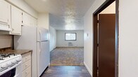 Located at 403 Greenbriar Dr in Normal, IL, this single-floor unit offers a straightforward, functional layout with a mix of hard-surface and carpeted flooring. The entry opens directly into a transitional zone where wood-look hard flooring connects the front door to the kitchen area. The kitchen is efficiently arranged, featuring white cabinetry, a white refrigerator, a range, and a sink, all set beneath recessed lighting. Painted white brick walls appear throughout the unit, lending a durable, textured character to the interior.

The living area flows naturally from the kitchen and entry, featuring carpet flooring, a textured ceiling, and a window with a wall-mounted HVAC unit beneath it, providing both natural light and climate control. The bedroom is a quiet, carpeted room with its own window fitted with blinds, a wall-mounted HVAC unit, and a closet with sliding doors offering built-in rod and shelf storage. The painted brick wall continues here, maintaining a consistent aesthetic.

The bathroom includes a full tub-and-shower combination with white tile surround and chrome fixtures, keeping the space clean and practical. Overall, the unit presents a no-frills, utilitarian design suited for straightforward, comfortable living.