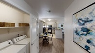 Located at the Atlas community in Las Vegas, Nevada, this single-floor residence offers a thoughtfully designed open-concept layout that connects the main living areas seamlessly. The living room features wood-look flooring, neutral walls, and ample space for comfortable seating, complemented by a dedicated dining area illuminated by a stylish pendant chandelier. Adjacent to the dining space, a louvered-door closet conceals a stacked in-unit washer and dryer — a practical convenience. The kitchen is well-equipped with gray shaker-style cabinetry, light countertops, black appliances including a gas range, microwave, and full-size refrigerator, and tile flooring that transitions cleanly into the living spaces. The primary bedroom is generously sized with plush carpet, a ceiling fan, large windows that invite natural light and outdoor views, and a walk-in closet with built-in shelving. The en-suite bathroom features tile flooring, a vanity with gray cabinetry, and a shower-tub combination. A secondary bedroom also offers carpet, a sliding door closet, and windows with outdoor views. The overall ambiance is clean, modern, and move-in ready, with a cohesive neutral palette throughout.