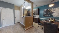 This single-floor residence offers a thoughtfully designed layout that balances modern style with everyday functionality. The kitchen is a standout feature, showcasing dark espresso cabinetry, white quartz countertops, a subway tile backsplash, stainless steel appliances including a refrigerator, microwave, and range, and wood-look vinyl flooring that extends throughout the main living areas. A half-wall peninsula with pendant lighting connects the kitchen to the dining area, which features a teal accent wall and pendant light fixture, adding a vibrant touch to the space. The living room provides a comfortable, open feel with warm neutral walls, wood-look flooring, and easy access to the rest of the home. Multiple bedrooms are present, each carpeted and distinguished by bold navy or dark accent walls that lend a modern, dramatic character. The primary bedroom benefits from natural light through a large window and features ample space. Each bathroom includes a full soaking tub and shower combination with white tile surround, and the primary bath offers a vanity with a large mirror and wood-tone cabinetry. Throughout the residence, a consistent palette of warm beige tones, dark wood finishes, and teal and navy accents creates a cohesive and contemporary aesthetic.