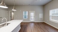 Located at 13100 Margie Ln in Raleigh, NC, this thoughtfully designed one-bedroom, one-bathroom unit offers a modern living experience across a single floor. The open-concept layout seamlessly connects the kitchen, dining, and living areas, maximizing functionality and flow. The kitchen is a standout feature, boasting light wood-grain cabinetry, crisp white quartz countertops, a classic subway tile backsplash, and a full suite of stainless steel appliances including a refrigerator, range, and built-in microwave. A central island with pendant lighting serves as both a prep space and casual dining area. Rich wood-look flooring runs throughout the main living areas, complementing the neutral gray tones of the walls. The living area is bright and airy, with a glass-panel door leading directly to a private patio. The bedroom features plush carpet flooring, a ceiling fan, and a window that brings in natural light. The bathroom is finished with clean subway tile in a frameless glass walk-in shower with brushed nickel hardware. Additional conveniences include a dedicated laundry area, a utility room, and a closet for storage.