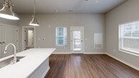 Located at 13100 Margie Ln in Raleigh, NC, this thoughtfully designed one-bedroom, one-bathroom unit offers a modern living experience across a single floor. The open-concept layout seamlessly connects the kitchen, dining, and living areas, maximizing functionality and flow. The kitchen is a standout feature, boasting light wood-grain cabinetry, crisp white quartz countertops, a classic subway tile backsplash, and a full suite of stainless steel appliances including a refrigerator, range, and built-in microwave. A central island with pendant lighting serves as both a prep space and casual dining area. Rich wood-look flooring runs throughout the main living areas, complementing the neutral gray tones of the walls. The living area is bright and airy, with a glass-panel door leading directly to a private patio. The bedroom features plush carpet flooring, a ceiling fan, and a window that brings in natural light. The bathroom is finished with clean subway tile in a frameless glass walk-in shower with brushed nickel hardware. Additional conveniences include a dedicated laundry area, a utility room, and a closet for storage.