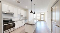 This well-appointed 2-bedroom, 2-bathroom residence offers a thoughtfully designed single-level layout that maximizes both comfort and functionality. The open-concept kitchen serves as the heart of the home, showcasing crisp white shaker cabinets, a white subway tile backsplash, granite countertops, and a suite of stainless steel appliances including a refrigerator, range, and dishwasher. A central kitchen island with a matching granite surface provides additional prep space and is illuminated by a pair of industrial-style pendant lights. Light wood-look flooring flows seamlessly from the kitchen through the main living area, which is bathed in natural light from large windows and a glass door at the far end. A stylish barn door adds a modern accent near the entryway. Both bedrooms are carpeted and feature ceiling fans, natural light from dual windows, and generous walk-in closets with built-in shelving and hanging rods. The bathrooms are cleanly finished, with one featuring a full tub-shower combination accented by white tile, granite-topped vanities, and wood-look flooring. The overall palette is bright and neutral, creating a clean, contemporary ambiance throughout.