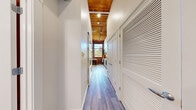 This one-bedroom, one-bathroom loft-style unit masterfully combines industrial heritage with contemporary design across a single, efficiently laid-out floor. A long entry hallway with wood-plank flooring and a warm wood-paneled ceiling with track lighting leads you into the heart of the space. Exposed red brick walls appear throughout, lending authentic character and texture that contrast beautifully with the crisp white walls and modern finishes. The open kitchen is well-appointed with light wood cabinetry, white quartz countertops, a stainless steel sink, and a full suite of stainless steel appliances including a range, microwave, dishwasher, and refrigerator. Large multi-pane windows flood the kitchen and dining area with natural light while offering views of the surrounding greenery. The living room features the same exposed brick corner detail and hardwood-style flooring, creating a cozy yet stylish atmosphere. The bedroom is an intimate, restful retreat with exposed brick accents, dark wood ceiling beams, and a sliding barn-style closet door. The bathroom is clean and modern, finished in white tile with a full tub-shower combination, wood-look flooring, and recessed lighting. Every room reflects a thoughtful balance of raw, historic character and polished, contemporary living.
