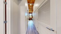 This one-bedroom, one-bathroom loft-style unit masterfully combines industrial heritage with contemporary design across a single, efficiently laid-out floor. A long entry hallway with wood-plank flooring and a warm wood-paneled ceiling with track lighting leads you into the heart of the space. Exposed red brick walls appear throughout, lending authentic character and texture that contrast beautifully with the crisp white walls and modern finishes. The open kitchen is well-appointed with light wood cabinetry, white quartz countertops, a stainless steel sink, and a full suite of stainless steel appliances including a range, microwave, dishwasher, and refrigerator. Large multi-pane windows flood the kitchen and dining area with natural light while offering views of the surrounding greenery. The living room features the same exposed brick corner detail and hardwood-style flooring, creating a cozy yet stylish atmosphere. The bedroom is an intimate, restful retreat with exposed brick accents, dark wood ceiling beams, and a sliding barn-style closet door. The bathroom is clean and modern, finished in white tile with a full tub-shower combination, wood-look flooring, and recessed lighting. Every room reflects a thoughtful balance of raw, historic character and polished, contemporary living.