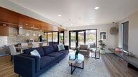 Located at 1714 NW Overton St in Portland, Oregon, this single-floor space presents a thoughtfully designed, open-plan layout that blends contemporary aesthetics with functional versatility. The expansive main living area is defined by wood-look flooring, recessed lighting, and multiple distinct seating zones. A standout linear fireplace is set into a floor-to-ceiling travertine-tiled surround, creating a commanding focal point along one wall. Adjacent to it, a floating media console provides additional functionality. A second seating area features a large sectional sofa and curated wall art, offering a more intimate lounge setting.

Natural light fills the space through generous windows and a set of dark-framed French doors that open directly to an outdoor patio area, providing views of lush greenery. The fully equipped kitchen is a refined workspace, featuring dark wood cabinetry, stainless steel appliances including a range, dishwasher, and large refrigerator, white quartz countertops, and a distinctive geometric mosaic tile backsplash. A warm wood-paneled ceiling in the kitchen zone adds a rich architectural contrast. A breakfast bar with seating completes the kitchen area. Throughout, the design maintains a cohesive modern palette of warm neutrals and natural materials.
