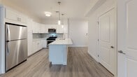 This single-floor residence at 674 Dartmouth Street in Dartmouth, MA, presents a clean, modern design throughout. The open-concept living and dining area is finished with light wood-look flooring and neutral walls, creating a bright, welcoming atmosphere. Natural light filters in through windows fitted with white blinds, enhancing the airy feel of the space.

The kitchen is a functional centerpiece, featuring white shaker-style cabinetry extending to the ceiling, a white center island with a built-in sink, light gray tile backsplash, and stainless steel appliances including a gas range, microwave, and refrigerator. Pendant lighting above the island adds a polished finishing touch.

The carpeted bedrooms are finished in soft neutral tones with clean white baseboards. One bedroom includes access to a well-organized walk-in closet with built-in shelving and hanging rods. Two bathrooms serve the unit: one features a tub-shower combination with subway tile surround, light tile flooring, a white vanity, and accessibility grab bars; the second offers a similar white vanity with a mirror and cabinet above, also with light tile flooring. The overall ambiance is contemporary, clean, and move-in ready.