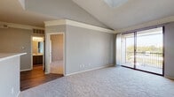 This single-floor residence offers a thoughtfully designed layout with a blend of comfort and functionality. The main living area immediately impresses with its vaulted ceilings accented by a clean white crown molding ledge, creating a sense of heightened volume and openness. Soft, neutral-toned carpet covers the living space, while sliding glass doors lead to a private balcony, flooding the room with natural light and offering pleasant outdoor views. The front entry door opens directly into this airy living space, reinforcing the open and welcoming feel.

The galley-style kitchen features dark gray cabinetry, white appliances including a range, microwave, dishwasher, and refrigerator, along with wood-look flooring and a pass-through window that connects to the living area, maintaining visual continuity throughout the space.

The bedrooms are generously sized, each finished with plush carpet, ceiling fans, and ample natural light from well-placed windows. The primary bedroom benefits from direct access to a private en-suite bathroom, which is outfitted with dark gray vanity cabinetry, a quartz-style countertop, wood-look flooring, and a tiled shower-tub combination. The overall color palette of soft grays and neutral tones lends the space a clean, modern, and cohesive aesthetic throughout.