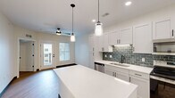 Located at 4591 McRee Ave in St. Louis' vibrant Tower Grove neighborhood, this thoughtfully designed one-bedroom, one-bathroom unit delivers modern finishes and a highly functional layout. The open-concept kitchen serves as the heart of the home, showcasing white shaker cabinetry with matte black hardware, quartz countertops, a teal subway tile backsplash, stainless steel appliances, and a central island with pendant lighting—ideal for both cooking and entertaining. Light wood-tone flooring flows seamlessly throughout, tying the living and kitchen areas together. A glass door leads to a private outdoor balcony, filling the space with natural light. The spacious bedroom features a ceiling fan, a window for additional natural light, direct access to a walk-in closet with wire shelving, and a connecting door to the full bathroom. The bathroom is finished with a white vanity, quartz countertop, wood-look flooring, and a walk-in shower with white tile surround and a sliding glass door with black hardware. A dedicated laundry area accommodates a full-size washer and includes utility connections. Clean white walls, recessed lighting, and consistent black accent hardware throughout lend the space a cohesive, contemporary aesthetic.