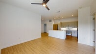 This well-designed single-story, 3-bedroom, 2-bathroom home in Boerne, TX offers a thoughtful layout that balances functionality and modern aesthetics. The open-concept living and kitchen area serves as the heart of the home, featuring warm light wood-style flooring, recessed lighting, and a ceiling fan. The kitchen is equipped with stainless steel appliances, a subway tile backsplash, shaker-style cabinetry in a neutral tone, a central island with a white countertop, and pendant lighting — ideal for both everyday cooking and entertaining. A hallway connects the main living space to the private quarters, highlighted by a frosted glass accent door that adds a contemporary touch. The three bedrooms are generously proportioned, with the primary bedroom offering notable space. Bedrooms feature plush carpeting, ceiling fans, and windows that allow natural light and outdoor views. The bathrooms are clean and modern; one features an ADA-accessible roll-in shower, floating vanity, and grab bars. Additional spaces include five closets, a laundry room, a utility room, and a patio. The overall design presents a bright, neutral palette suited for comfortable living.