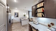 Located in Tomball, Texas, this thoughtfully designed one-bedroom, one-bathroom residence offers a smart and efficient single-floor layout. The open-concept kitchen and living area serves as the heart of the home, featuring granite countertops, rich dark-toned cabinetry, and stainless steel appliances including a full-size refrigerator. A peninsula with pendant lighting doubles as a prep and dining space, while a built-in desk nook with open shelving provides a dedicated workspace. Wood-look plank flooring runs throughout the main living areas, adding warmth and continuity. The living room is bathed in natural light from oversized windows dressed with horizontal blinds and dark drape panels, complemented by a ceiling fan overhead. The bedroom offers a cozy retreat with plush carpeting, a ceiling fan, a large window, and a walk-in closet. The bathroom is finished with a granite vanity, dark cabinetry, wood-look tile flooring, and a subway-tiled tub-shower combination. Clean white walls and recessed lighting throughout create a bright, modern ambiance that makes the space feel open and inviting.