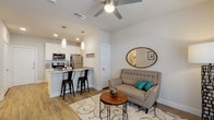 This single-story residence is designed with a clean, contemporary aesthetic, featuring an open-concept layout that seamlessly connects the kitchen and living area. Wood-look flooring runs throughout, lending warmth and continuity to the space.

The kitchen is well-appointed with white shaker cabinetry, quartz countertops, a tile backsplash, and a full suite of stainless steel appliances, including an electric range, over-the-range microwave, dishwasher, and refrigerator. A peninsula with an undermount sink and pendant lighting above serves as both a functional workspace and a casual dining spot with bar seating.

The living area is bright and inviting, with a ceiling fan overhead and natural light entering through glass French doors. The space is compact yet functional, offering room for a seating arrangement and accent furnishings.

A full bathroom features large-format tile surrounding a soaking tub and shower combination, white cabinetry for storage, and wood-look flooring that complements the rest of the unit. The 3D floor plan also reveals a separate bedroom area, providing a private retreat. Overall, the unit presents a cohesive, modern interior with neutral tones and practical finishes throughout.