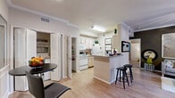 This thoughtfully designed 1-bedroom, 2-bathroom residence offers a functional and comfortable single-floor layout. The open-concept kitchen and living area serves as the heart of the home, featuring light wood-style flooring, crown molding, and a ceiling fan that enhances the bright, airy atmosphere. The kitchen is well-equipped with white appliances, including a range, microwave, refrigerator, and dishwasher, complemented by granite-style countertops and a peninsula breakfast bar with barstool seating — ideal for casual dining. A pantry closet and additional storage are conveniently located nearby. The living room opens directly onto a private balcony through sliding glass doors, offering a pleasant outdoor retreat with views of the surrounding landscaping. The spacious bedroom features carpeted flooring, a ceiling fan, and direct access to a walk-in closet and an en-suite bathroom. A second full bathroom serves guests and the common areas. Both bathrooms are appointed with granite-style countertops and large mirrors. The unit also includes an in-unit laundry area. Throughout the residence, crown molding and neutral tones create a cohesive and welcoming ambiance, making this a well-rounded and efficiently designed living space.
