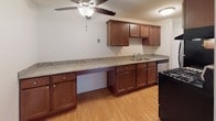 This single-floor unit offers a practical and comfortable layout designed for everyday living. The open living area is finished with warm hardwood-style flooring that extends throughout, and large sliding glass doors lead to a private balcony, flooding the space with natural light and providing outdoor views. A ceiling-mounted air conditioning unit and baseboard heating ensure year-round comfort.

The kitchen is a standout feature, showcasing rich dark wood cabinetry, generous granite-style countertops that extend along a wide workspace, a stainless steel sink, and black appliances including a gas range. A ceiling fan adds both style and functionality to the kitchen area.

The bedrooms are carpeted for warmth and comfort. One bedroom includes a built-in closet with a full-width rod and shelving, offering ample storage. Natural light filters in through windows fitted with vertical blinds, and baseboard heaters line the walls.

The bathroom is clean and efficiently designed, featuring a full soaking tub with an overhead shower, a toilet, and a vanity topped with a granite-style countertop set into warm wood cabinetry. Tile-style flooring completes the space. Overall, the unit presents a cohesive, move-in-ready environment with practical finishes throughout.