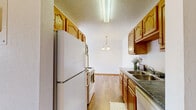 Located at 1717 40th St S in Fargo, North Dakota, this one-bedroom, one-bathroom unit offers a well-organized, single-floor layout designed for comfortable everyday living. The galley-style kitchen is outfitted with warm oak cabinetry, dark granite-style countertops, a double-basin sink, and white appliances including a coil-top range, refrigerator, and over-the-range microwave. Durable hardwood-style flooring runs the length of the kitchen, which opens toward the combined dining and living area. The living and dining space is carpeted and bathed in natural light, with a pendant light fixture overhead and a sliding glass door that leads to a private balcony, offering outdoor access and additional light. Baseboard heating and a wall-mounted air conditioning unit ensure year-round comfort. The bedroom is a generously sized, carpeted retreat featuring a large window with natural light, a mirrored sliding-door closet, and warm wood trim throughout. The unit also benefits from three total closets for ample storage. The full bathroom includes a tiled tub-and-shower combination and tile flooring. A textured ceiling is present in the kitchen and bathroom areas, while the living spaces feature clean, smooth white walls throughout.