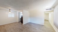 This single-floor unit offers a clean, functional layout finished with light wood-style flooring and crisp white walls throughout. The open living area is bright and welcoming, benefiting from natural light streaming through windows dressed with vertical blinds. A ceiling fan adds comfort to the space, while a textured ceiling provides a classic finishing detail carried consistently across the main living areas. The kitchen is thoughtfully designed in a galley-style configuration, featuring white upper cabinetry, light countertops, a black electric range, a dishwasher, and a refrigerator. An arched pass-through opening connects the kitchen to the living area, maintaining an open, airy feel while defining the spaces. The bedroom is generously proportioned and includes two side-by-side closets, one of which is open-shelved, providing ample storage. A textured ceiling and the same light flooring continue into this room. The unit includes two bathrooms: one full bath with a shower-tub combination, white vanity cabinetry, and wood-style flooring; and a second bathroom featuring a vanity, toilet, and dual towel bars. Both bathrooms are finished in a clean, neutral palette. Overall, the unit presents a practical and well-maintained interior with a cohesive, light-toned aesthetic.