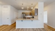 This 1-bedroom, 1-bathroom residence offers a thoughtfully designed open-concept layout with a seamless blend of comfort and modern finishes. The living area features light wood-style flooring, a ceiling fan, and a glass-paneled door that invites natural light and provides access to an outdoor balcony, creating an airy and welcoming atmosphere.

The kitchen is a standout feature, anchored by a peninsula with a granite countertop and bar seating illuminated by two geometric pendant lights. Warm-toned cabinetry pairs with stainless steel appliances — including a refrigerator, range, and microwave — while a subway tile backsplash adds a clean, contemporary touch.

The bedroom is a comfortable retreat finished with soft carpeting, a ceiling fan, and a large window overlooking the surrounding neighborhood. A set of double bi-fold closet doors provides ample storage. The bathroom is efficiently designed with granite vanity countertops, gray cabinetry, wood-look tile flooring, and a full tub-shower combination.

Additional features include a dedicated hallway, a closet, and a carpeted staircase with a handrail leading to the unit's entry. The neutral color palette and consistent finishes throughout create a cohesive and move-in-ready living space.