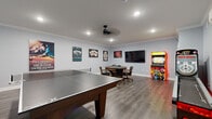 Located at 705 Newark Ave in Elizabeth, NJ, this dedicated game room is a fully outfitted entertainment haven designed for fun and social gatherings. The single-floor space offers a comfortable, open layout with wood-look flooring, crisp white crown molding, and light gray walls that create a clean, modern backdrop for its eclectic array of recreational amenities.

At the center of the room sits a full-size ping-pong table, commanding the main floor area with ample room for play on all sides. A round poker table surrounded by padded gaming chairs anchors one corner, complemented by a large wall-mounted flat-screen TV — ideal for watching games or movies between rounds. A colorful vintage-style arcade cabinet adds a nostalgic touch, while a skee-ball machine with LED underglow lighting brings additional arcade energy to the space.

The walls are adorned with an eclectic mix of pop culture and gaming-themed artwork, including movie posters and poker-inspired prints, lending the room a lively, personalized character. Recessed ceiling lighting and a ceiling fan ensure the space remains well-lit and comfortable during extended use. A wall-mounted mini-split HVAC unit provides independent climate control. The overall ambiance is energetic yet polished — a purpose-built retreat for entertainment.