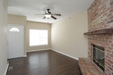 This two-story home is designed with a practical and comfortable layout spread across both levels. The main level begins at a welcoming entryway with dark hardwood flooring and a ceiling fan overhead. The open living area is a standout space, anchored by a full brick fireplace that adds warmth and character. The living area flows toward the kitchen, which features white cabinetry with dark hardware, dark granite-style countertops, a double-basin stainless steel sink, and white appliances including a range and built-in microwave. Hardwood flooring continues throughout the main level. A carpeted staircase with a handrail connects to the upper floor. The upper level hosts multiple bedrooms, each finished with plush neutral carpet and ceiling fans. The bedrooms are generously sized and include ample closet space, with at least one room featuring a walk-in closet. A full bathroom on this level includes a soaking tub, tile flooring, and a vanity with sink. An additional bathroom with tile flooring is also present. Neutral warm-beige tones are consistent throughout, contributing to a clean and cohesive ambiance.