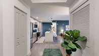 This single-story residence at 10550 SW Innovation Way in Port St. Lucie, FL presents a contemporary open-concept design highlighted by wood-look flooring, elevated ceilings, and a cohesive color palette anchored by deep slate-blue accent walls. The living area is a welcoming focal point, featuring a ceiling fan, large-scale artwork, and sliding glass doors that open onto a private balcony with outdoor views, filling the space with natural light.

The kitchen is thoughtfully designed with light wood cabinetry, stainless steel appliances, a white waterfall-edge island with bar seating, and sleek pendant lighting overhead. The layout flows seamlessly into the living and dining areas, making it well-suited for everyday living and entertaining.

The bedroom offers a calm, neutral atmosphere with direct access to a walk-in closet and a private bathroom. The bathroom features an extended vanity with light wood cabinetry, a wide LED-backlit mirror, and white countertops, creating a clean and functional space. An in-unit laundry closet with a full-size washer and dryer adds everyday convenience. Throughout, the design balances modern finishes with a warm, livable aesthetic.