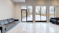 Located at 95 Thorncliffe Park Drive in Toronto, this single-floor multi-purpose space offers a generous and versatile layout across its entire footprint. The main hall is a standout feature, boasting a distinctive coffered ceiling with recessed grid lighting that evenly illuminates the expansive, open floor area. Light-toned ceramic tile flooring runs throughout, creating a clean and cohesive aesthetic. A grand piano positioned in the corner hints at the hall's suitability for performances, gatherings, or community events. Adjacent to the main hall is a bright lounge area characterized by high ceilings, glossy white tile flooring, and large floor-to-ceiling windows and glass doors that frame views of the tree-lined outdoor surroundings, flooding the space with natural light. Comfortable seating is provided for visitors. The fully equipped kitchen features rich dark-wood cabinetry, black appliances including a full-size refrigerator, stove, and dishwasher, tiled walls, and ample counter and storage space, making it well-suited for catering and event support. A connecting hallway with additional cabinetry and a second refrigerator extends the kitchen's functionality. The entry corridor provides practical access between areas and includes multiple utility controls. Overall, the space presents a functional and welcoming environment ideal for community programming and events.