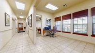 Located at 5201 James Ave in Fort Worth, TX, this single-floor community clubhouse offers a well-appointed gathering space designed for both relaxation and recreation. The layout flows naturally from a bright, open lounge area finished with neutral-toned tile flooring, crown molding, and elegant touches including a ceiling fan, recessed lighting, and framed artwork. The lounge provides comfortable seating arranged around a coffee table, creating an inviting atmosphere for socializing.

A dedicated computer workstation area features a granite-topped desk, task seating, and multiple windows dressed with rich wooden Roman shades, allowing natural light to fill the space. Skylights in the ceiling further enhance brightness throughout the common areas and connecting hallway.

The game room is a standout feature, anchored by a classic wooden pool table set atop plush carpeting. A wall-mounted flat-screen television, ceiling fan, and additional seating at small tables make this room ideal for leisure and entertainment. Skylights here also contribute to a light and airy ambiance.

A connecting hallway lined with framed artwork and large mirrors ties the spaces together, leading to additional areas including what appears to be a kitchenette. Overall, the clubhouse presents a warm, functional, and community-oriented environment suited for residents to gather, work, and unwind.