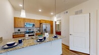 This thoughtfully designed one-bedroom, one-bathroom residence in Greeley, Colorado offers a practical and attractive layout across a single floor. The kitchen serves as the centerpiece of the living space, featuring warm honey-toned wood cabinetry extending to the ceiling, granite countertops, and a full suite of stainless steel appliances including a side-by-side refrigerator with ice maker, electric range, over-the-range microwave, and dishwasher. A peninsula with pendant lighting overhead provides additional prep and dining space, while light hardwood-style flooring ties the area together seamlessly. A hallway connects the main living areas to the private quarters. The bedroom is a comfortable, carpeted retreat bathed in natural light from a window fitted with blinds, and includes access to a dedicated closet. The full bathroom is finished with warm wood vanity cabinetry, a granite-topped vanity with a large mirror, hardwood-style flooring, and a full shower-tub combination. Clean white walls and neutral tones throughout the residence create a bright, cohesive ambiance, making this an efficient and well-appointed living space.