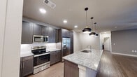 This single-story, 2-bedroom, 2-bathroom residence in Round Rock, TX offers a well-designed layout with modern finishes throughout. The open-concept kitchen and living area serves as the heart of the home, anchored by a generous granite-topped island with an integrated sink and pendant lighting above. Dark-toned shaker cabinetry, a white subway tile backsplash, and a full suite of stainless steel appliances—including a French door refrigerator, electric range, and microwave—complete the kitchen. Wood-look flooring runs through the main living areas, contributing to a clean, contemporary aesthetic.

Both bedrooms are carpeted and offer a quiet, comfortable atmosphere. The primary bedroom includes a walk-in closet outfitted with multi-tier shelving and hanging rods for organized storage, and a ceiling fan for added comfort. The second bedroom also features a ceiling fan and a window with exterior views. Each bathroom is distinctly appointed: one features a tiled soaking tub and shower combination, while the other offers a glass-enclosed walk-in shower, both with dark-finish vanities topped with granite countertops and wood-look flooring.