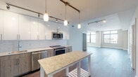 Located at 33 Monroe St in Rockville, MD, this contemporary single-floor residence offers a thoughtfully designed open-concept layout with a seamless flow between the kitchen and living areas. The kitchen is a standout feature, showcasing a two-tone cabinet design with crisp white upper cabinets and warm wood-toned lower cabinets, a classic subway tile backsplash, stone countertops, and a full suite of stainless steel appliances including a range, microwave, dishwasher, and refrigerator. Pendant lighting and track lighting illuminate the space with a modern touch, while dark hardwood flooring anchors the entire living area with warmth and elegance. The living room is bathed in natural light from expansive floor-to-ceiling windows that frame sweeping views of the Rockville cityscape, creating a bright and airy atmosphere. The bedroom features plush carpeting, clerestory windows, and direct access to a generously sized walk-in closet with multi-level wire shelving for ample storage. Two well-appointed bathrooms complete the unit — one featuring large-format tile flooring, a wood-toned vanity with stone countertop, and a soaking tub, while the other offers a dual-sink vanity with light wood cabinetry and large tile flooring. This residence combines modern design with functional living in the heart of Rockville.