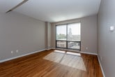 This single-floor residence features a thoughtfully designed open-concept layout that seamlessly connects the kitchen and living areas. The kitchen is a standout space, outfitted with rich dark wood cabinetry extending to the ceiling, stainless steel appliances including a refrigerator, range, and built-in microwave, and light-toned countertops. A central island with a double sink and integrated dishwasher serves as both a functional workspace and a natural divider between the kitchen and the living area. Warm pendant lighting with amber-toned shades hangs above the island, adding a welcoming ambiance.

The living area is bright and airy, benefiting from a large floor-to-ceiling window that frames outdoor views and floods the space with natural light. Warm-toned hardwood flooring flows throughout the main living areas, complementing the neutral gray walls. A bedroom features plush carpeting and its own window with natural light, while a second room with hardwood floors provides additional versatile space. The bathroom is finished with tile flooring, a dark wood vanity with a light countertop, a mirrored medicine cabinet, and contemporary brushed nickel fixtures, completing this well-appointed residence.