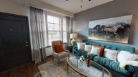 This single-story residence at Springs At Hamburg offers a thoughtfully designed layout with distinct living spaces that balance functionality and contemporary style. The living room serves as a focal point, showcasing gray accent walls, wood-look flooring, and large windows dressed with elegant floor-to-ceiling drapes that invite generous natural light. A ceiling fan adds both comfort and visual interest overhead.

The kitchen is outfitted with dark espresso cabinetry, granite countertops, and a full suite of stainless steel appliances, including a refrigerator, electric range, and built-in microwave. A dedicated dining area accommodates a round wooden table and features wood-look flooring, with convenient access to the in-unit laundry room, which houses a full-sized top-loading washer and dryer.

The bedrooms are carpeted for comfort, each featuring natural light through blinds-fitted windows and ceiling fans. The bathroom includes a granite-topped vanity with dark cabinetry, wood-look flooring, and a full soaking tub with shower combination. Throughout the residence, a cohesive neutral palette with bold accent tones creates a welcoming and polished atmosphere.