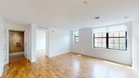 Located at 1702 Summit Pl NW in Washington, DC's vibrant Adams Morgan neighborhood, this 2-bedroom, 1-bathroom residence offers a clean, modern aesthetic throughout. Warm honey-toned hardwood floors run continuously across every room, complementing bright white walls and crisp white baseboards for a cohesive, contemporary look.

The open-plan kitchen and living area serves as the heart of the home, featuring sleek white cabinetry with under-cabinet lighting, modern appliances, and recessed lighting overhead. Large black-framed windows flood the living space with natural light and offer views of the surrounding neighborhood.

Both bedrooms are well-proportioned and finished with the same hardwood flooring. The primary bedroom benefits from multiple windows that bring in generous sunlight, while the second bedroom includes a built-in sliding-door closet for convenient storage. Each room maintains a clean, minimalist character ideal for a variety of furnishing arrangements.

The bathroom is thoughtfully designed with large-format neutral tile flooring, floor-to-ceiling tile in the walk-in glass shower with a rainfall showerhead, and a streamlined white vanity. A hallway connects the living areas to the bedrooms and provides access to two closets, adding practical storage throughout the unit.