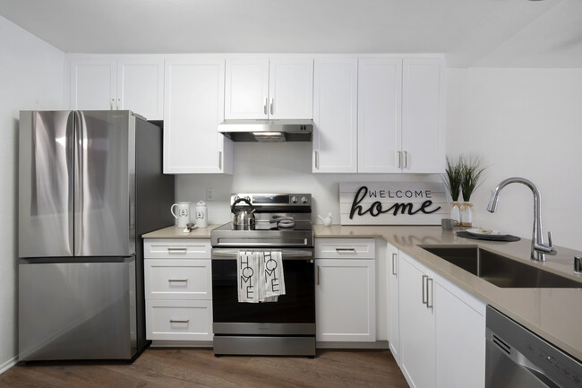 Renovated Package I kitchen with stainless steel appliances, light grey quartz countertops, white cabinetry, and hard surface flooring - eaves Phillips Ranch