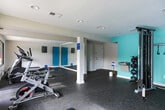 This single-level fitness center in Marietta, Georgia, offers a comprehensive workout environment designed to accommodate a range of exercise routines. The space is divided into distinct functional zones, each thoughtfully arranged to maximize usability. Durable rubber flooring throughout provides both safety and comfort during workouts.

The cardio area is equipped with treadmills, elliptical machines, and a stationary cycling bike. Large windows along this section of the facility allow abundant natural light to filter in and provide direct views of an outdoor pool area, creating an engaging atmosphere during exercise.

A dedicated strength and flexibility zone features a cable machine, a two-tier dumbbell rack with a selection of free weights, a stability ball, and an adjustable workout bench. A vibrant teal accent wall adds a distinct visual character to this section. Full-length wall mirrors are integrated into the space, enhancing the sense of openness while allowing users to monitor their form.

An additional open area provides space for stretching and mat-based exercises, supported by mounted yoga mats stored along the walls. A water fountain and hand sanitizer station are conveniently accessible within the facility. Recessed lighting and a climate control system contribute to a comfortable and well-maintained workout environment year-round.