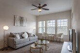 This single-floor residence offers a well-designed layout with a warm, neutral aesthetic throughout. The living area serves as the heart of the space, featuring plush carpeting, a ceiling fan, and an abundance of natural light streaming through multiple large windows with horizontal blinds. The open arrangement comfortably accommodates both a seating area and a dining nook, creating a versatile and inviting atmosphere.

The kitchen is outfitted with dark espresso cabinetry contrasted by light granite countertops and a subway tile backsplash. Stainless steel appliances, including a refrigerator, electric range with microwave, and dishwasher, provide modern functionality. Wood-look flooring runs throughout the kitchen, adding warmth and durability.

The bedroom is a tranquil retreat with carpet flooring, a ceiling fan, and a generously sized window that allows soft natural light to filter in. The room offers ample space for furnishings and provides a comfortable, restful environment.

The bathroom features dark wood cabinetry paired with a granite-topped vanity, a large mirror, and wood-look flooring. A shower-tub combination with a curtain rod completes the space. Overall, the residence presents a cohesive, contemporary design with practical finishes and a bright, airy ambiance.