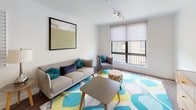 This thoughtfully designed 2-bedroom, 2-bathroom residence offers a cohesive, modern aesthetic across its single-floor layout. The kitchen is a standout feature, showcasing two-tone cabinetry with sleek flat-front doors in taupe and dark brown, white quartz countertops, a subway tile backsplash, and a full suite of stainless steel appliances including a refrigerator, electric range, microwave, and dishwasher. Wood-look flooring runs throughout the main living areas, lending warmth and continuity to the space. The open living and dining area is bright and inviting, anchored by a large window that allows natural light to fill the room. The living space comfortably accommodates a sofa, armchair, and coffee table, while the adjacent dining area features a wooden table with seating for several guests. In-unit stacked laundry adds a practical convenience. The primary bedroom features plush carpeting, a window with a roller shade, and ample room for a full-size bed and furnishings. The second bedroom is equally functional, accommodating a bunk bed setup with carpeted flooring. Both bathrooms are finished with wood-toned vanities, white countertops, and a tub-shower combination with sliding glass doors, maintaining the unit's clean, contemporary style throughout.