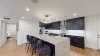 This thoughtfully designed single-floor residence blends modern aesthetics with functional living. The centerpiece of the home is a striking gourmet kitchen, outfitted with dark shaker-style cabinetry that reaches the ceiling, light granite countertops, and a sparkling mosaic tile backsplash. A generously sized island with an integrated sink provides ample seating for multiple guests and serves as a natural gathering point. Stainless steel appliances, including a French door refrigerator, range, microwave, and a sleek wall-mounted range hood, complete the chef's workspace. Warm hardwood flooring flows throughout, unifying the open layout. An artistic loop pendant light above the island adds a contemporary sculptural touch. The living area is bright and inviting, featuring crown molding, recessed lighting with integrated LED cove accents, and a ceiling fan. The space is anchored by a large wall-mounted television and accented by bold large-format artwork. Two well-appointed bedrooms offer ceiling fans, natural light through zebra-shade windows, and a calm, restful ambiance. The bathroom is elegantly finished with intricate Moroccan-pattern tile in the shower-tub combination, marble-style wall tile, granite vanity countertops, and dark accent cabinetry, creating a refined and spa-like retreat.