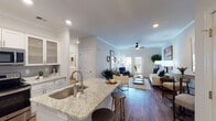 Located at 5300 High Point Rd in Greensboro, NC, this single-floor residence offers a thoughtfully designed open-concept layout that seamlessly connects the kitchen, dining, and living areas. The interior is finished with warm hardwood-style flooring that extends throughout the main living spaces, complemented by crown molding and recessed lighting that add a refined touch.

The kitchen is a standout feature, boasting white shaker-style cabinetry extending to the ceiling, light granite countertops, a gray tile backsplash, and a full suite of stainless steel appliances. A peninsula with an undermount sink and bar seating connects the kitchen to the living area, enhancing the open flow. Glass-front upper cabinets provide an elegant display element.

The living room is bright and inviting, with a ceiling fan, French doors allowing natural light, and ample space for comfortable seating. Two bedrooms offer carpeted floors and generous natural light from large windows. The primary bedroom includes an en-suite bathroom, while a second full bathroom features a tub-shower combination. A separate half bath with a granite-topped vanity provides added convenience. The overall ambiance is clean, modern, and welcoming.