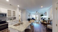 Located at 5300 High Point Rd in Greensboro, NC, this single-floor residence offers a thoughtfully designed open-concept layout that seamlessly connects the kitchen, dining, and living areas. The interior is finished with warm hardwood-style flooring that extends throughout the main living spaces, complemented by crown molding and recessed lighting that add a refined touch.

The kitchen is a standout feature, boasting white shaker-style cabinetry extending to the ceiling, light granite countertops, a gray tile backsplash, and a full suite of stainless steel appliances. A peninsula with an undermount sink and bar seating connects the kitchen to the living area, enhancing the open flow. Glass-front upper cabinets provide an elegant display element.

The living room is bright and inviting, with a ceiling fan, French doors allowing natural light, and ample space for comfortable seating. Two bedrooms offer carpeted floors and generous natural light from large windows. The primary bedroom includes an en-suite bathroom, while a second full bathroom features a tub-shower combination. A separate half bath with a granite-topped vanity provides added convenience. The overall ambiance is clean, modern, and welcoming.