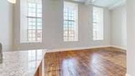 Located at 133 Tripp St in Fall River, MA, this 2-bedroom, 1-bathroom residence showcases a thoughtful blend of historic character and modern updates. Original wide-plank hardwood floors run throughout, adding warmth and a sense of history to the space. The open living and kitchen area is anchored by dramatically tall ceilings and a striking row of large, floor-to-ceiling windows that flood the room with natural light and offer views of the surrounding neighborhood. A structural column adds an industrial loft-like charm to the living area. The kitchen features warm wood cabinetry, granite countertops, stainless steel appliances including a side-by-side refrigerator and range, and a peninsula with pendant lighting and a built-in sink — ideal for both cooking and entertaining. The two bedrooms are calm and well-proportioned, with neutral walls and the same rich hardwood flooring; the primary bedroom includes a closet with built-in shelving. Three closets total provide ample storage throughout. The full bathroom is cleanly finished with a granite-topped vanity, tiled flooring, and a tub/shower combination. Two hallways connect the layout efficiently, completing this well-appointed and characterful residence.