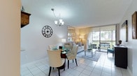 This single-floor residence offers a cohesive, light-filled interior defined by neutral tones, white tile flooring, and textured ceilings throughout the main living areas. The open-concept living and dining space is anchored by a chandelier above a glass-top dining table and flows seamlessly into the living room, which features a built-in shelving unit and a large sliding glass door that opens to a private balcony. The balcony overlooks lush greenery and palm trees, bringing natural light and outdoor views into the heart of the home.

The kitchen is outfitted with white cabinetry, granite countertops, and a full suite of white appliances, including a range, built-in microwave, and dishwasher, all complemented by white tile flooring. A pass-through connects the kitchen to the dining area for added convenience.

The bedrooms are carpeted and generously sized, with one bedroom offering direct balcony access. The bathroom features white cabinetry with a granite vanity, a glass-enclosed shower with tile accents, and a skylight that enhances the bright, clean aesthetic. A dedicated laundry closet with a stacked washer and dryer adds practical functionality to this well-appointed residence.