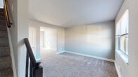 This two-floor home offers a well-organized layout designed for comfortable everyday living. The main level welcomes visitors through a front entry door into a carpeted living area bathed in natural light from a large front-facing window, offering views of the surrounding neighborhood. Adjacent to the living space is a functional kitchen equipped with warm honey-toned wood cabinetry, granite-style countertops, a stainless steel sink, and a black Whirlpool gas range, complemented by wood-look flooring that adds a clean, practical finish.

The upper floor hosts multiple carpeted bedrooms, each featuring neutral gray walls, windows with blinds that allow ample natural light, and generous closet space. One bedroom in particular benefits from a corner window configuration, providing added brightness and an exterior view of the neighborhood greenery. A full bathroom on this level includes a soaking tub with shower, tiled walls, wood-look flooring, and a towel bar, offering a straightforward and functional design.

Throughout the home, consistent neutral tones, white trim, and plush carpeting create a cohesive and move-in ready aesthetic. A staircase with a dark wood banister connects both floors, adding a classic architectural touch to the interior.