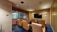 Located at 2080 FM 1102 in New Braunfels, Texas, this dedicated media room offers an intimate and thoughtfully designed screening experience. The single-room space is entirely clad in warm, light-toned wood paneling that wraps all four walls, creating a cohesive, cabin-inspired aesthetic that feels both inviting and acoustically refined.

The room is furnished with multiple tan leather lounge chairs arranged in a viewing configuration, each paired with a small round side table for added convenience. A large wall-mounted flat-screen television serves as the focal point, flanked by two sconce lights that provide warm, ambient illumination. Recessed ceiling lighting complements the overall atmosphere.

A built-in upholstered bench seat runs along one wall beneath a multi-pane black-framed window, offering additional seating and a view to an adjacent outdoor area. A dark wood cabinet beneath a framed artwork piece adds a decorative touch to one corner of the room.

Entry is provided through a striking black steel-framed glass door, clearly labeled as the Media Room. The rich, deep blue modular carpet grounds the space and provides a bold contrast to the natural wood tones above. Overall, this media room delivers a polished, comfortable, and functional environment well-suited for private screenings and small group gatherings.