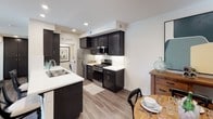 Located at 5002 Jewel St in Rocklin, California, this single-story residence offers a thoughtfully designed open-concept layout with modern finishes throughout. The kitchen is a standout feature, equipped with dark espresso cabinetry reaching to the ceiling, stainless steel appliances including a gas range and refrigerator, crisp white quartz countertops, and a central island with bar seating — all flowing seamlessly into the dining and living areas. Wood-style plank flooring runs throughout the main living spaces, adding warmth and continuity to the open floor plan. The living room is bright and welcoming, outfitted with a ceiling fan, a sliding glass door that opens to an outdoor patio, and generous natural light with views of the surrounding greenery. The primary bedroom features a tray ceiling, ceiling fan, plush carpeting, abundant natural light, a walk-in closet, and a private en-suite bathroom. The bathrooms are finished with dark vanity cabinetry, white countertops, large mirrors, and tub-shower combinations. A secondary bathroom mirrors the same contemporary styling. An in-unit washer and dryer area is conveniently integrated near the kitchen, adding practical everyday functionality to this well-appointed residence.