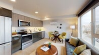 Located on the fifth floor at 701 5th Avenue North in Seattle's Lower Queen Anne neighborhood, this thoughtfully designed unit delivers a bright, modern living experience across a single level. The open-concept layout seamlessly connects the kitchen, dining, and living areas, creating an inviting and functional space. The kitchen is outfitted with stainless steel appliances — including a full-size refrigerator, electric range, microwave, and dishwasher — complemented by sleek two-tone cabinetry, a white subway tile backsplash, and clean countertops. A wall-mounted mini-split unit provides efficient climate control throughout the main living area. Light wood-style flooring flows throughout, enhancing the airy feel. The bedroom is a serene retreat featuring sliding closet doors and soft, neutral tones. A versatile den or flex room opens to a balcony through a glass sliding door, framing expansive views of the Seattle skyline and surrounding cityscape — a true highlight of the unit. The full bathroom features a clean, contemporary design with a wide vanity, wood-grain cabinetry, white quartz countertop, large mirror, and a tiled tub-shower combination. Recessed lighting and large windows throughout ensure the space is consistently filled with natural light.