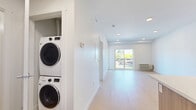 Located at 235 Hollywood Rd N in Kelowna, BC, this well-appointed one-bedroom, one-bathroom unit offers a thoughtfully designed layout across a single floor. Light-toned hardwood-style flooring flows throughout, complementing the bright, white walls and recessed lighting that create a clean, modern atmosphere.

The open-concept kitchen is a standout feature, anchored by a peninsula with wood-toned cabinetry and a crisp white countertop. Stainless steel appliances — including a refrigerator, electric range, and dishwasher — pair with a subway tile backsplash and white upper cabinets. Stylish matte black pendant lights add a contemporary touch overhead.

The living area extends naturally from the kitchen, benefiting from natural light that pours in through a large sliding glass door leading to a private balcony with pleasant outdoor views. A wall-mounted climate control unit ensures year-round comfort.

The hallway connects the main living spaces and includes an in-suite stacked washer and dryer, a highly practical addition. The bedroom is a calm, well-proportioned retreat featuring a sliding-door closet with built-in shelving for organized storage.

The bathroom is finished in a clean, all-white palette, featuring a full soaker tub and shower combination, a floating vanity with white countertop, and a large mirror, delivering a functional and contemporary feel throughout.