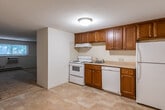 This single-floor unit offers a practical and straightforward layout designed for comfortable everyday living. The kitchen serves as a functional hub, featuring rich warm-toned wood cabinetry that extends both above and below the counter, providing ample storage. It is equipped with white appliances including an electric range, dishwasher, and refrigerator, complemented by light-toned countertops and easy-to-maintain tile flooring. A range hood overhead and a flush-mount ceiling light keep the space well-lit and ventilated.

The living area flows directly from the kitchen and is finished with neutral carpeting underfoot and a textured ceiling overhead. A large window allows natural light to fill the room while offering views of surrounding greenery. Baseboard heating and a wall-mounted air conditioning unit ensure year-round climate comfort.

The bedroom is a quiet, carpeted retreat featuring a sliding-door closet for organized storage. It connects seamlessly to the main entry area, which also benefits from baseboard heating. The bathroom includes a full-size tub and shower combination with a clean white surround, over-toilet cabinetry for additional storage, and classic fixtures. Throughout the unit, neutral tones and simple finishes create a clean, move-in-ready environment.