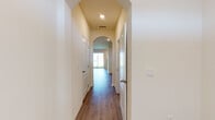 This two-story home offers a thoughtfully designed layout with consistent, modern finishes throughout both levels. The main floor features an open-concept living and kitchen area anchored by a staircase with a railed banister. The kitchen is well-equipped with crisp white shaker-style cabinetry, granite countertops, a subway tile backsplash, a peninsula with a built-in sink, and a full suite of stainless steel appliances including a refrigerator, range, and over-the-range microwave. A full bathroom on the main level includes a walk-in shower, granite vanity countertop, and hardwood-style flooring. Upstairs, a hallway with a distinctive arched passageway and recessed lighting connects multiple bedrooms, each featuring hardwood-style flooring, closet storage with built-in shelving, and access to adjoining rooms. A second full bathroom on this level includes a tub-shower combination, a granite-topped vanity, and coordinating flooring. Throughout the home, neutral warm-toned walls, white trim, and consistent hardwood-style flooring create a clean, cohesive aesthetic. The doll's-eye view of the layout reveals a spacious and well-proportioned floor plan designed for comfortable, functional living across both floors.